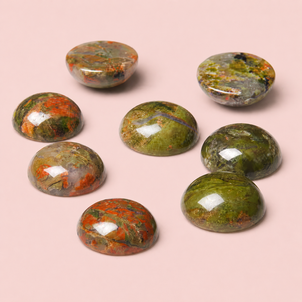 Nahaufnahme der grün und rot-braun marmorierten Unakit-Naturstein-Cabochons für das Hundehalsband Waldrose von Mops Berlin vor altrosafarbenem Hintergrund.