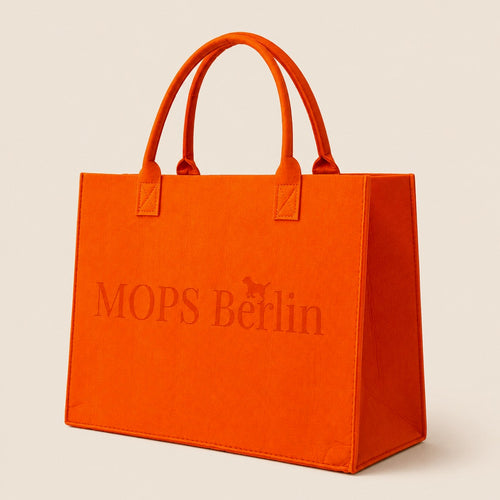 Schräge Seitenansicht der orangefarbenen Filztasche von MOPS Berlin mit eingeprägtem Logo und stabilen Tragegriffen vor hellem Hintergrund