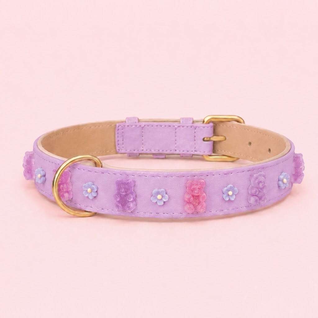 Quadratisches Produktfoto des Mops Berlin Hundehalsbands Zuckerwiese aus fliederfarbenem veganem Leder, verziert mit lila Gummibärchen- und Blumen-Applikationen sowie goldener Schnalle und D-Ring vor rosa Hintergrund.