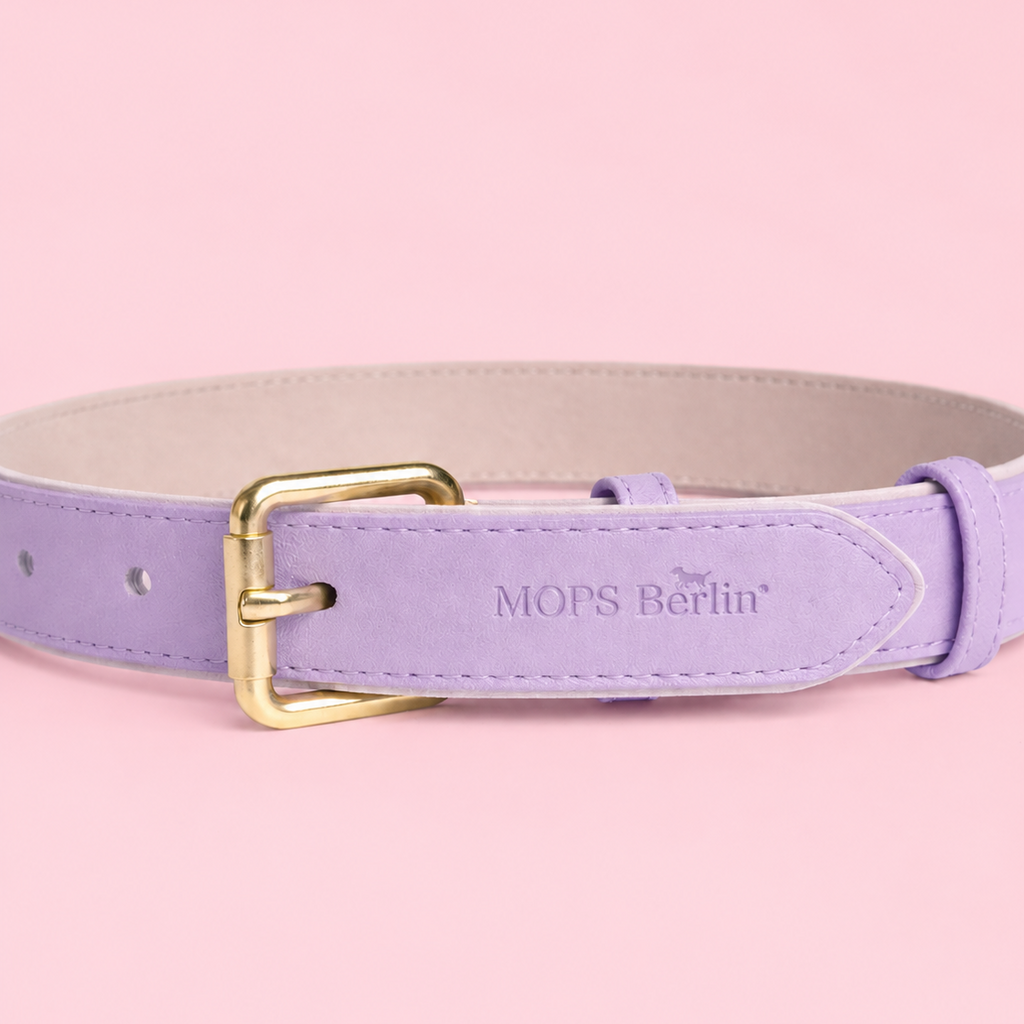 Nahaufnahme vom Schnallenende des Mops Berlin Hundehalsbands Zuckerwiese aus fliederfarbenem veganem Leder mit eingeprägtem Logo und mattgoldener Metallschließe vor rosa Hintergrund