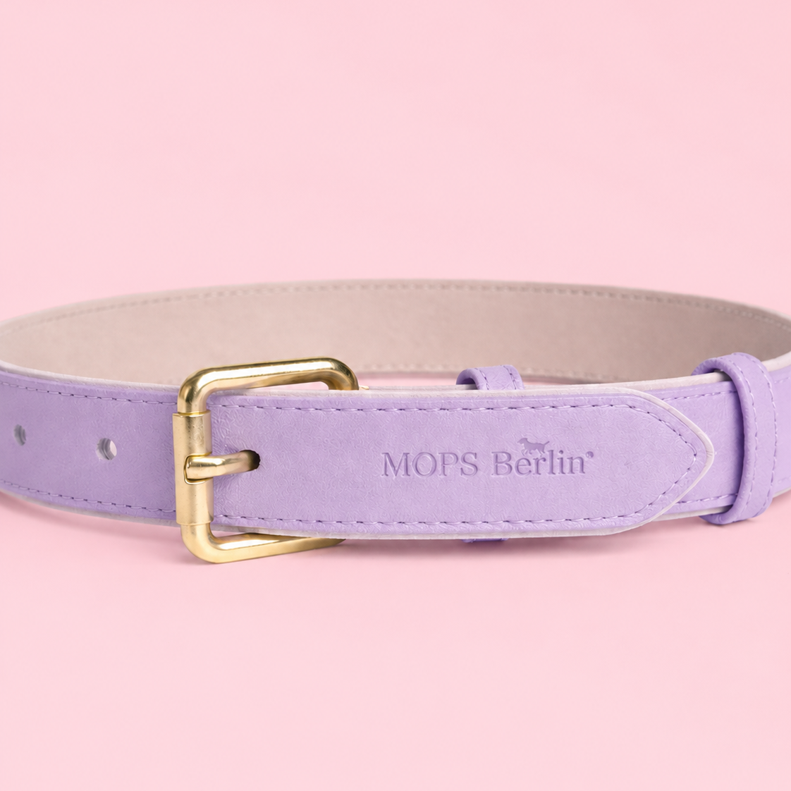 Nahaufnahme vom Schnallenende des Mops Berlin Hundehalsbands Zuckerwiese aus fliederfarbenem veganem Leder mit eingeprägtem Logo und mattgoldener Metallschließe vor rosa Hintergrund